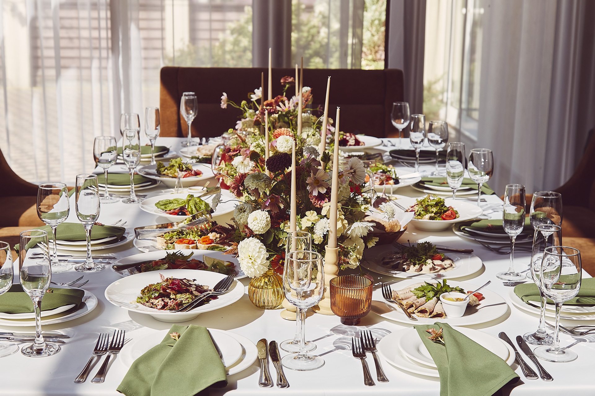 A formal dining table set with green napkins, floral centerpiece, candles, glassware, and plates of assorted salads and appetizers.